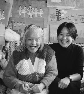 Black and white image of two women sitting in front of a wall of art.