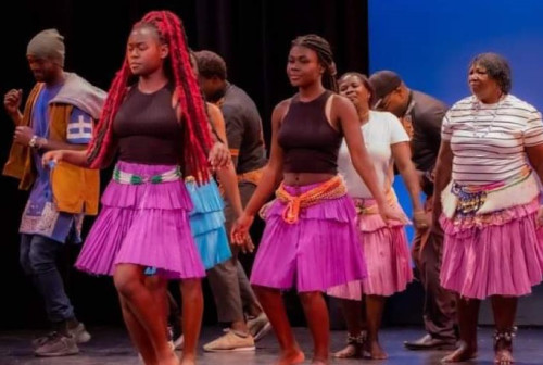 A group of people dance on stage at the Diversity Festival. About eight people, wearing colourful clothes, are pictured. One woman at the front has long red hair and is captured mid-dance move