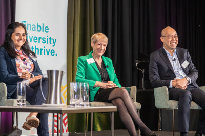 Photo of three people sitting on chairs on a stage, smiling.